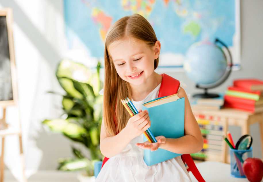 meine‑schulkiste.de - ein Kind mit Schulsachen im Klassenzimmer, im Hintergrund steht eine Weltkarte, Globus, Tafel und eine Pflanze